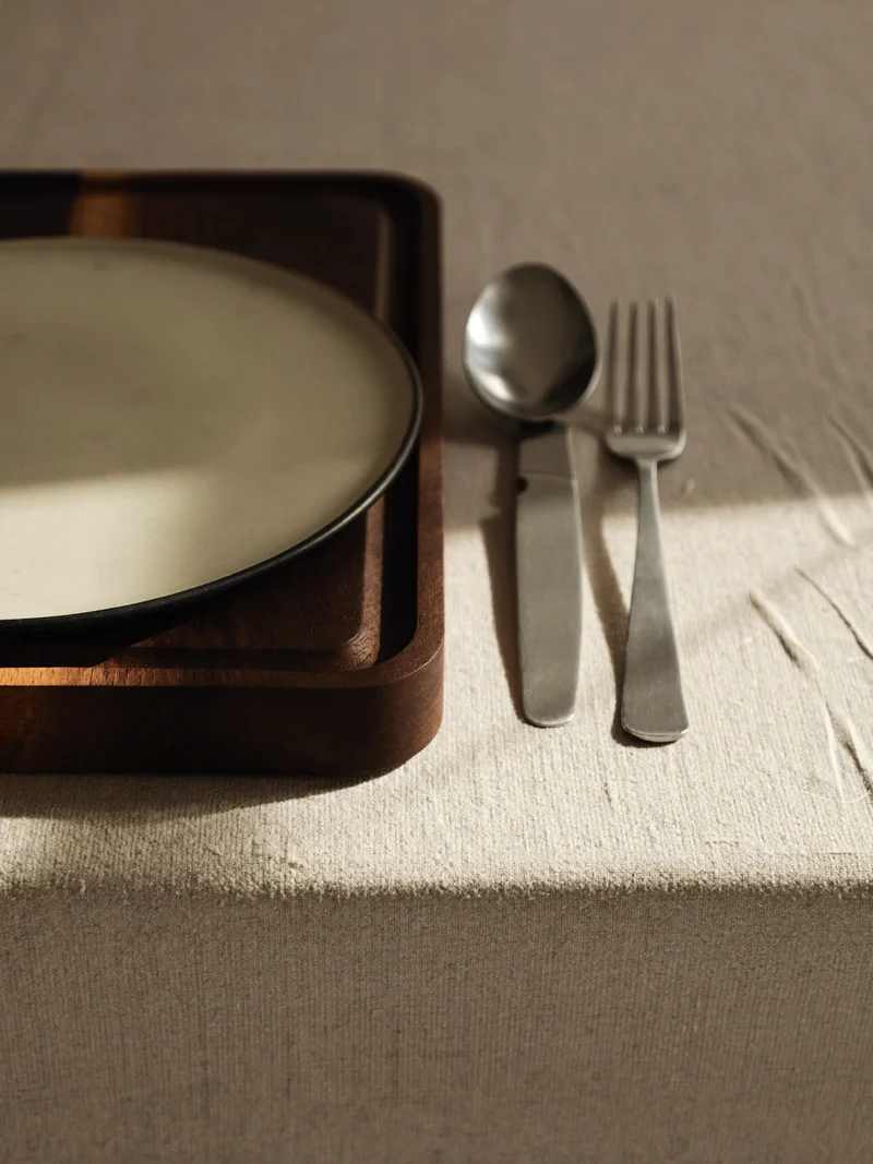 Tagliere in noce, piatto in ceramica e posate su tovaglia di lino, vista dall'alto